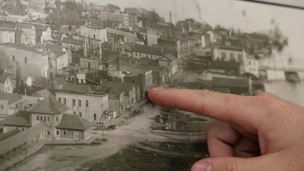 A finger points at a factory building from an old 1894 aerial photo of Manitowoc