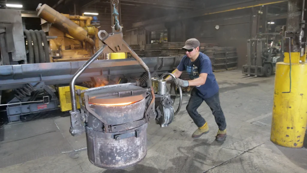 An employee pushes a large pot of molten metal